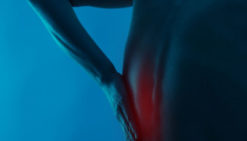 Man holds pain in the left side of his back during spasm.