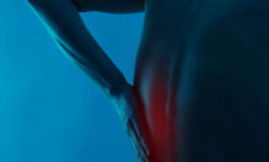 Man holds pain in the left side of his back during spasm.